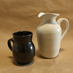 A tall, white pitcher and a large, black mug