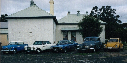 Picture of some of the Bordertown Vehicle Restorers Club members' cars in front of the old school complex Clubrooms