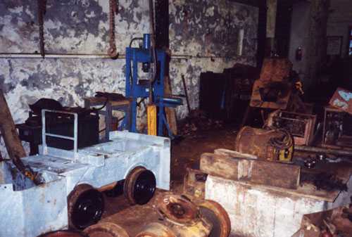Loco chasis with wheels and motor fitted in the Loco repair shop. In the background is an Hydraulic Press at South Crofty.