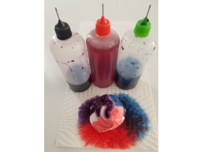 Three small bottles of liquid dye with needle point caps. I dolip of shaving cream in front with liquid dye dripped on it