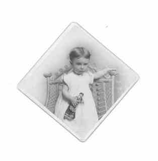 
Milly (hair parted in the middle) standing with small doll in left hand

