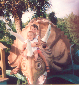 James and Josh riding a triceratops at the miniature golf course