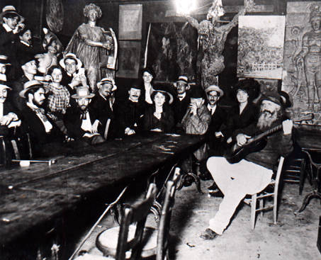 Inside the Lapin Agile.  Frd is sitting on the right with a guitar; on the wall to the left of the large crucifix is the Picasso painting "Au Lapin Agile."