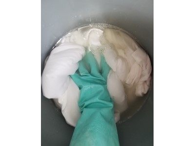 A bucket filled with soda ash with a hand agitating the sheet that is soaking