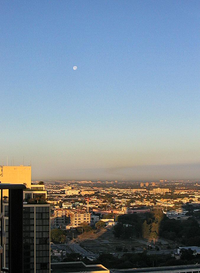 Sunrise lights the city on Thursday morning, while a mostly full moon hangs in the sky.