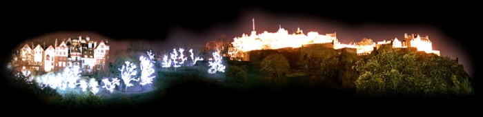 Edinburgh Castle lit up alongside a row of illuminated trees and Old Town buildings on the downward slope of Castle Hill.