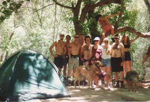 A group of tourists pose in their campsite.  The dogs in the picture are natives who exchange nightly protection from animals for tidbits of the campers food.