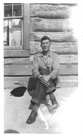 Higgins? Unidentified man sitting in front of a log cabin