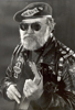Man with berret, dark glasses, and leather jacket with patches hold Bible