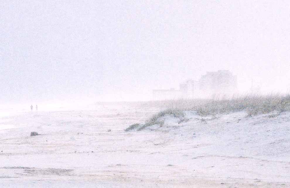 Soft focus beach scene with partly fog concealed condiminiums in the right back ground. Small figures walking on beach to left.