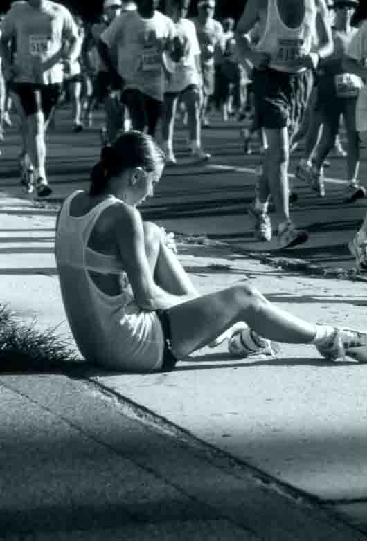 Woman sitting on ground in pain as runners pass by.