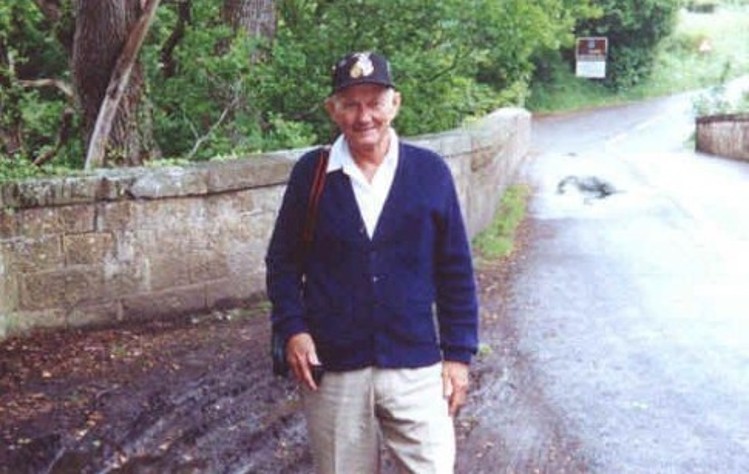 William Loren (Bill) Liddell stands at the opening to the Liddel River bridge just south of the border of England and Scotland.  The sign in the far distance alongside the road marks the border.  