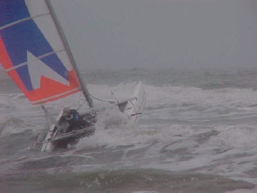 Skipper wasting time on setting his lee rudder in thesurf. thus risking a capsize
