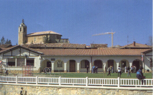 Las antiguas escuelas, los columpios y la iglesia al fondo
