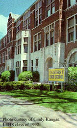 Eastern High School: "A view of the front of the school.  Here the school faces west.  We are looking NNE at the two center entrances.  A blue and yellow sign is visible on the lawn, identifying the school."