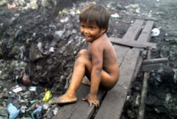 A child shyly smiles as he sits on a footbridge connecting two mountains of garbage in an ulingan in Hapilan, Tondo, Manila.