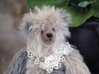 Tilly is made from two different colors of sparse mohair, teal and sage green. She has bent legs for sitting and glass eyes. She's wearing a neckpiece of vintage lace and buttons. Tilly is 10" tall.