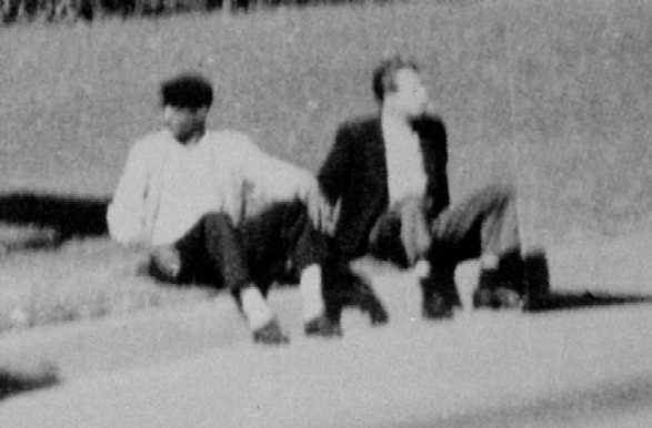The dark complected man (left) and umbrella man (right) sit on the curb seemingly uneffected by the events that had just taken place
