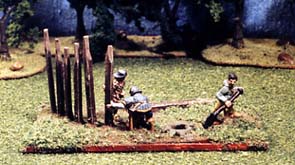 A camp follower digs holes for posts that two soldiers are erecting for a medieval camp