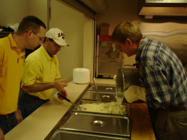 PGK Jason Doke and FS Jerry Hays help Dave Lake pour the mash potatoes into the serving line