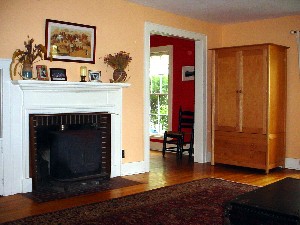 Living room w three floor-to-ceiling windows, wood stove and entrance to dining room and hall