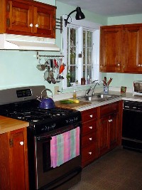 Kitchen with cherry cabinets, new gas/electric stove, two windows, and door to covered porch and deck