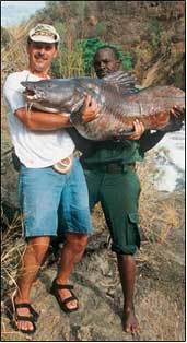 A TOURIST AND A HELPER SHOW OFF A PRIZE CATCH OF NILE PERCH