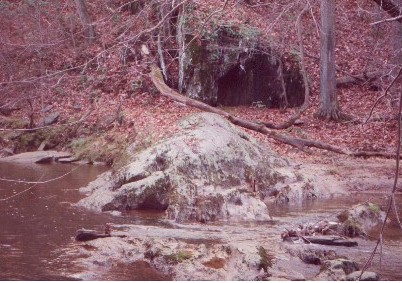 A mossy rock jutting out into the stream, with a foreboding black rock face behind it.