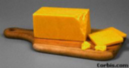 A large block of chease on a cutting board with a knife and seveal slices suggesting that it has be cut.