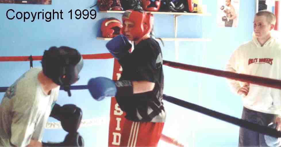 Outside the ring, a young boxer watches the sparring.&nbsp; He is still learning the basics and has yet to enter the ring, but will soon!&nbsp; He can learn much by watching the match and listening to the the critique of the coach.&nbsp; Image copyright 1999.&nbsp; All rights reserved.
