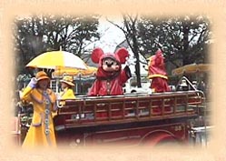 Mickey Mouse, in rain coat, waving from a fire engine 
on Main Street