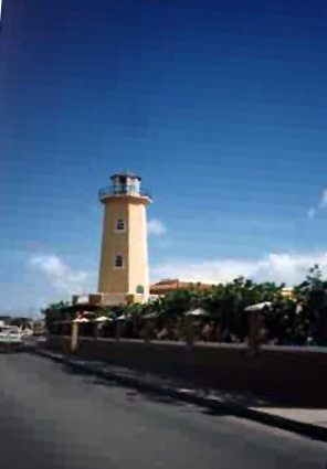 A tan colored lighthouse against the blue sky a road is at the bottom.