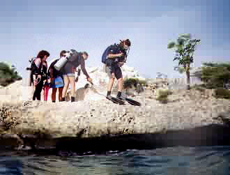 4 scuba divers ready to jump into the water from a small distance from the surface