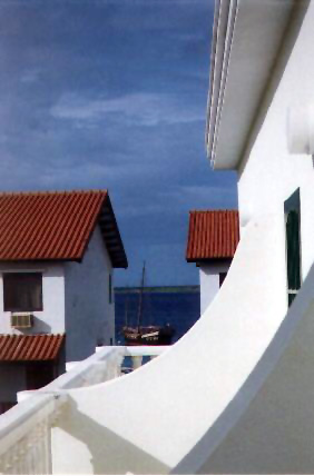 An old sailboat in the distance with two white buildings framing it from the sides.
