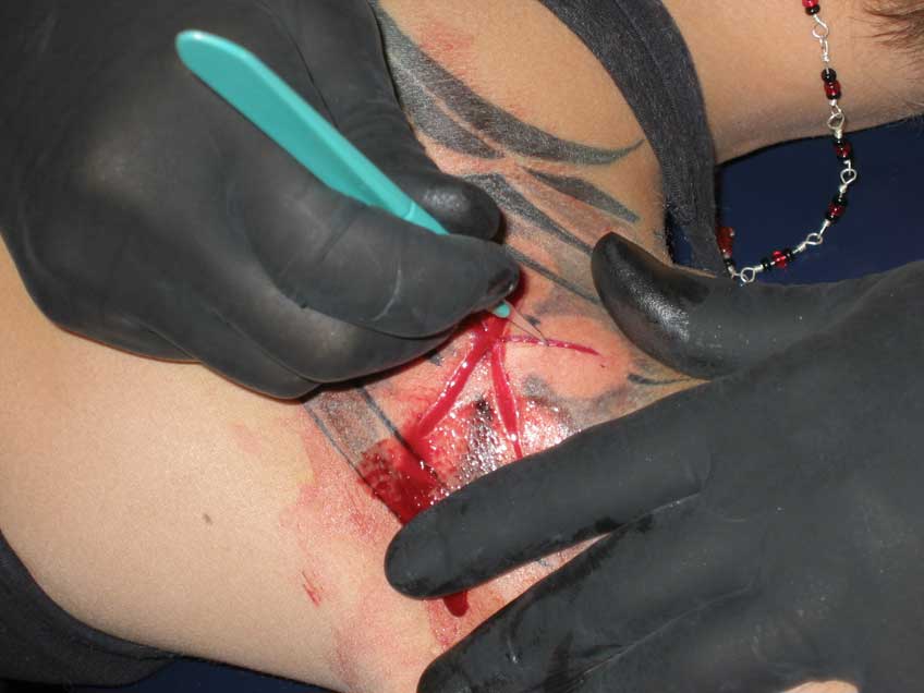 Buzz is doing scarification or cutting a design into the skin, the design has been worked into her tattoo - DO NOT TRY THIS AT HOME!!!!!
