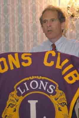 Past president Phil Grimaldi "stands" behind the podium and speaks about the history of the Little Brown Jug game.