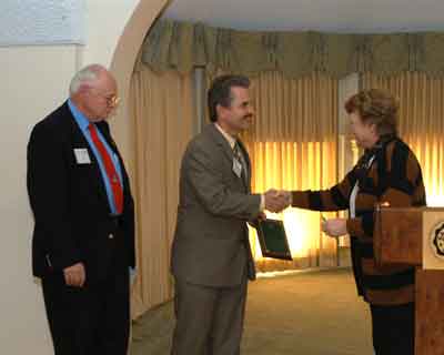 Lion Ted Rapson receives the Beautification Award from Marcia Schmidt of the Saginaw Branch of the Woman's National Farm and Garden Association, as Lion Wil Hufton looks on.