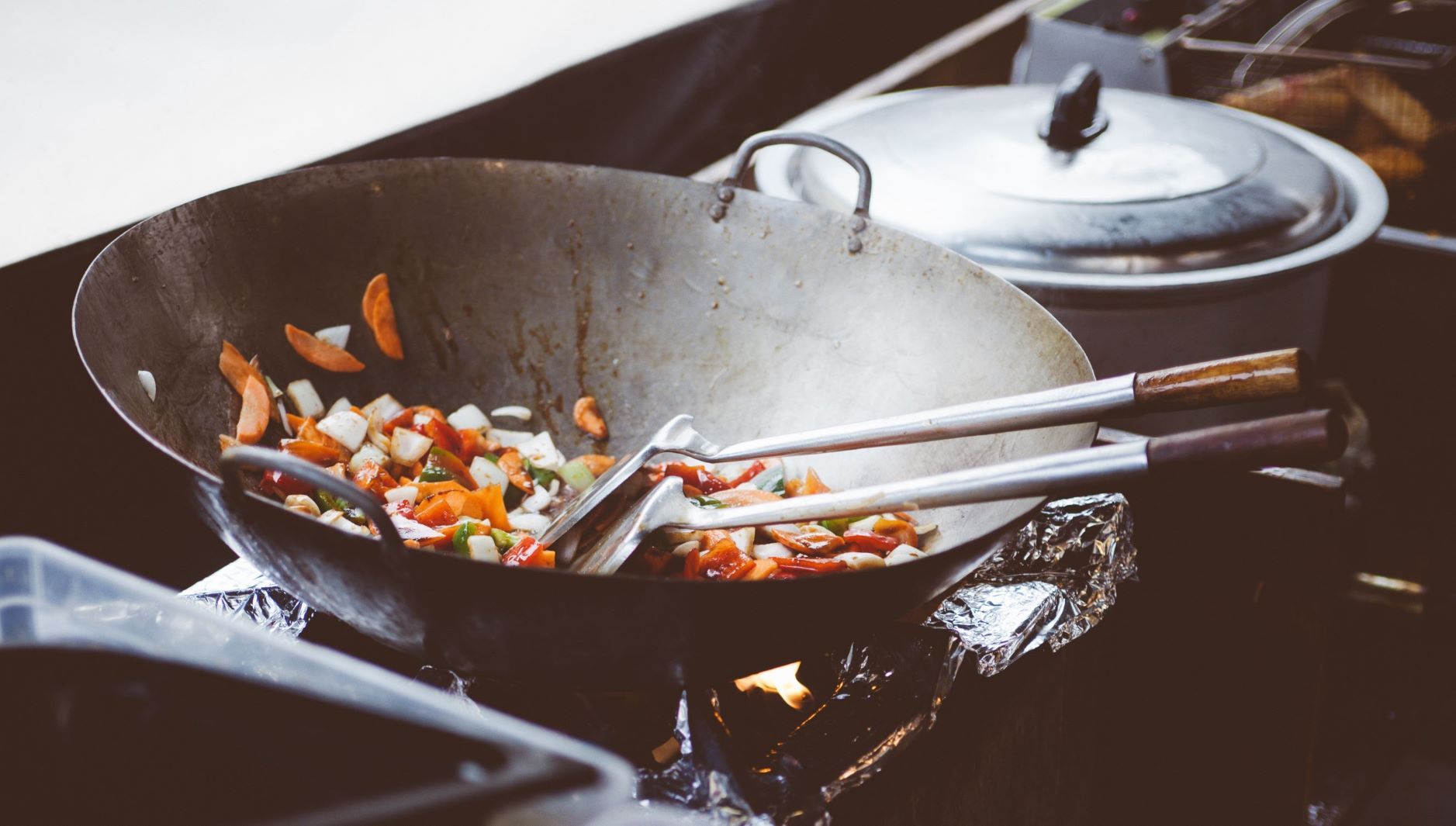 Food in a cooking wok with spatula on a grill with tongs
