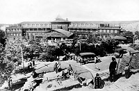 EL TOVAR AS SEEN FROM THE ROOF OF HOPI HOUSE.  NATIVE EMPLOYEES POSING ON DIFFERENT LEVELS OF ROOF. FRED HARVEY TOURING CARS PARKED AROUND ENTRANCE LOOP. CIRCA 1922. FRED HARVEY PHOTO