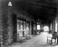 E PORCH & MAIN ENTRANCE OF EL TOVAR HOTEL, MAN & WOMAN SITTING ON VERANDA. CIRCA 1905. DETROIT PHOTOGRAPHIC. 