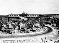 WIDE ON THE FRONT OF EL TOVAR HOTEL FROM THE  ROOF OF HOPI HOUSE. UNPAVED DRIVEWAY, WOOD BOARDWALK & NATIVE VEGETATION (THINNED SINCE EARLIER PHOTOS) 1907