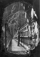 LOOKING THROUGH TRAIL TUNNEL ON S SIDE OF COLORADO RIVER ONTO THE KAIBAB BRIDGE. PARK NATURALIST, EDWIN MCKEE,  STANDS IN PROFILE AT THE RAILING. 17 JUNE 1949. NPS, GRANT. 