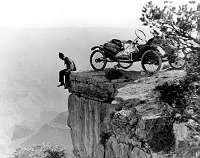 THE METZ AUTO PARKED AT THE RIM OF THE CANYON. DRIVER IS SEATED ON THE EDGE WITH HIS LEGS HANGING OVER THE CLIFF. CIRCA 1914. WING. 