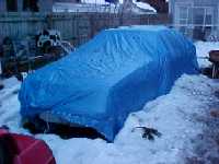 The Mustang in winter, encased in a car cover and tarp in the backyard